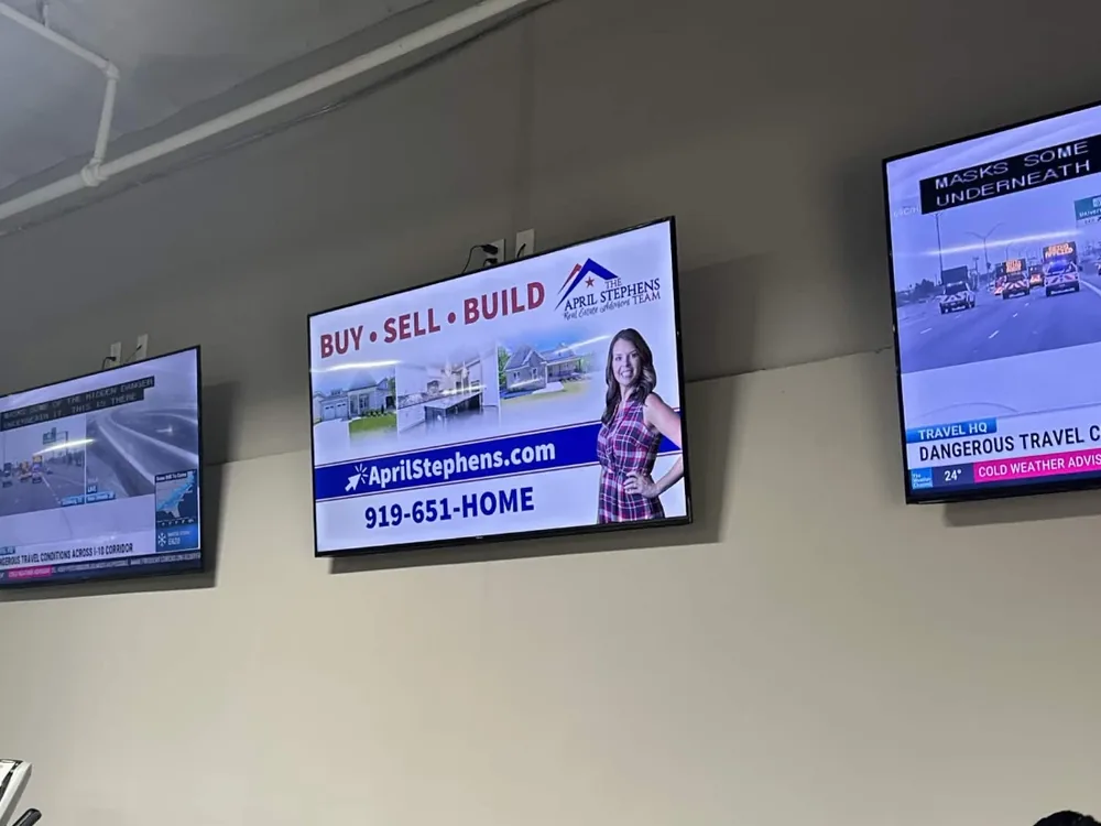 Gym screen wall where one display runs an April Stephens real estate ad alongside live TV