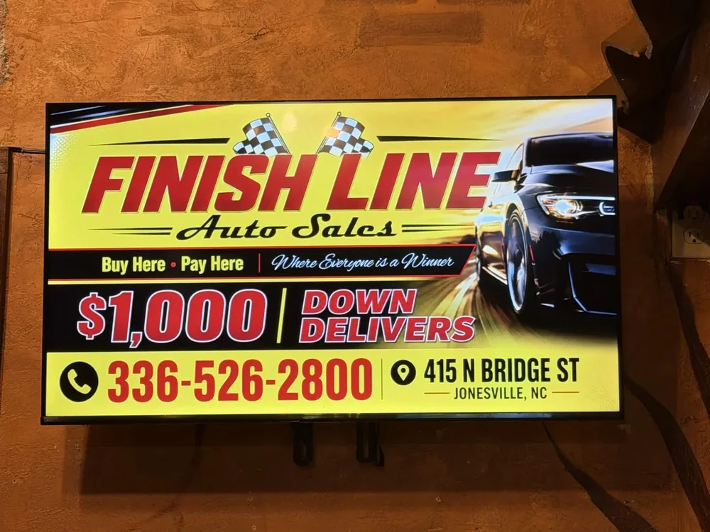 Wall-mounted digital billboard running a Finish Line Auto Sales ad inside a restaurant